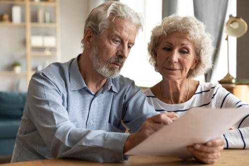 An older man and woman sit together at a table, closely reading and discussing a document.