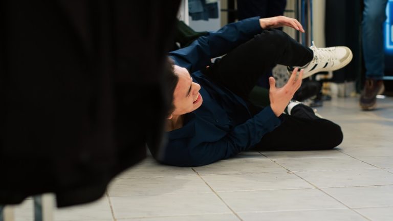 Person lying on the floor of a store, appearing to be in pain and holding their knee, possibly after slipping or falling.