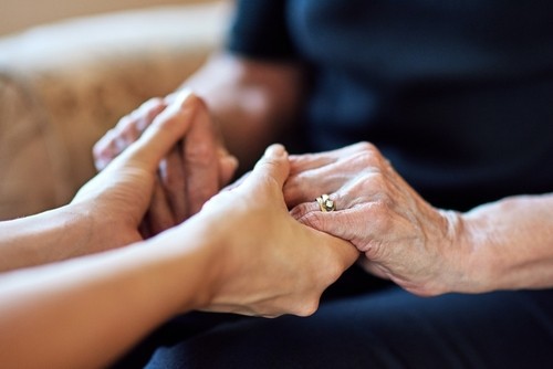 Close-up of two people holding hands, one appearing older and wearing a wedding ring, suggesting comfort or support.