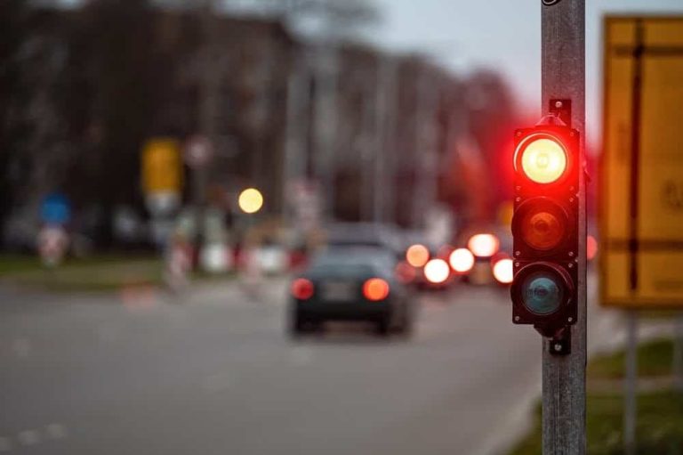 A traffic light shows red at an intersection with blurred cars and street signs in the background.