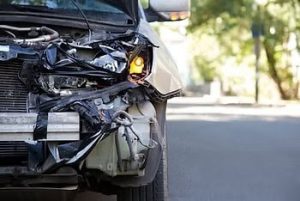 Front view of a damaged car with a crumpled hood and a broken headlight on a street.
