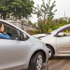 Two cars have collided head-on at low speed on a road. Both drivers remain seated in their vehicles, appearing to look at each other after the accident.