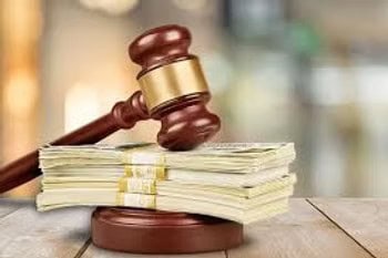 A judge's gavel rests on a wooden block next to several stacks of cash on a table.