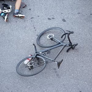 A bicycle lies on its side on the pavement next to a person’s legs and helmet.