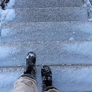 Person wearing boots and light-colored pants stands at the top of outdoor steps covered with snow and ice.