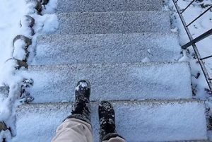 Person wearing boots walking down snowy steps outdoors.