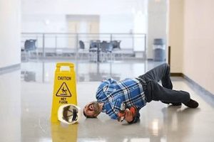 Man in plaid shirt slipping on wet floor next to a caution sign in a hallway, holding a mop.