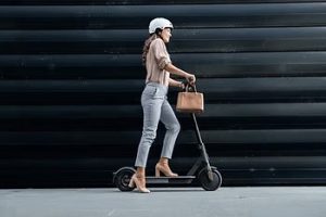 Person in a helmet riding an electric scooter while holding a handbag against a dark striped background.