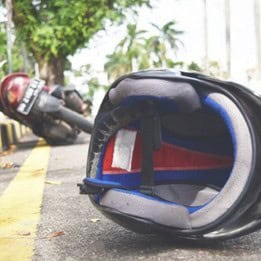 A motorcycle lies on its side near a curb, with a helmet positioned in the foreground on the pavement.