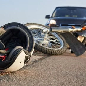 A motorcycle and helmet lie on the road in front of a car, suggesting a recent traffic accident.