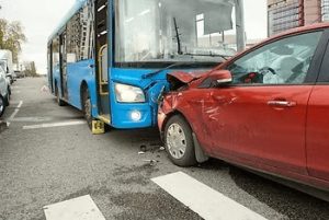 A red car collides with the front of a blue bus at an intersection, causing visible damage to both vehicles.