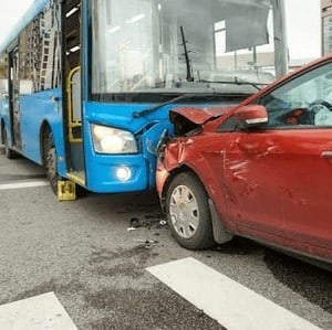 A red car and a blue city bus are involved in a collision at an intersection, both vehicles showing visible damage.