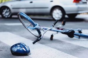A bicycle and helmet are lying on a crosswalk near a car on the road.