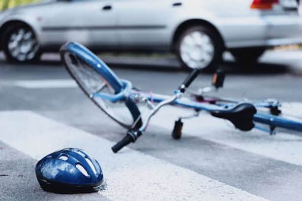 A blue bicycle and helmet lie on a crosswalk near a silver car, suggesting a recent accident or collision.