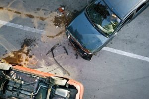 Overhead view of two cars involved in an accident on a road, one flipped over with visible damage and debris scattered around them.