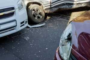 Three cars are involved in an accident, with noticeable damage and debris scattered on the road. One vehicle is white, another is red, and the third is black and white.