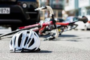 A white bicycle helmet lies on the road near a fallen bicycle and a black car, suggesting a possible accident scene.