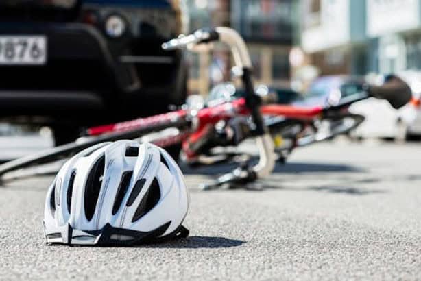 A white bicycle helmet lies on the road near a fallen bicycle and a black car, suggesting a possible accident scene.