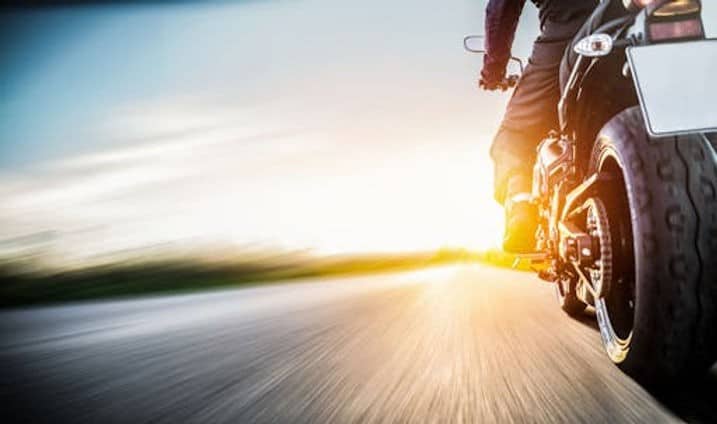 A person rides a motorcycle on a road at sunset, with motion blur emphasizing speed.