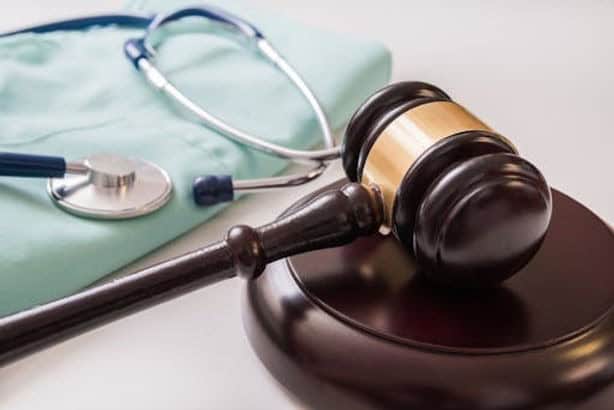 A judge’s gavel and block are placed next to medical scrubs and a stethoscope, symbolizing legal issues in healthcare.