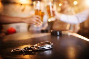 A set of car keys lies on a bar counter while four people in the background raise glasses of beer for a toast.