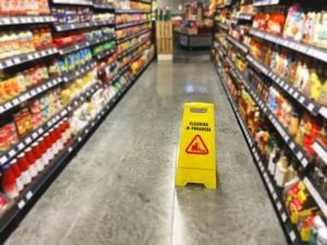 A yellow "Cleaning in Progress" sign stands in the aisle of a grocery store between shelves stocked with various products.