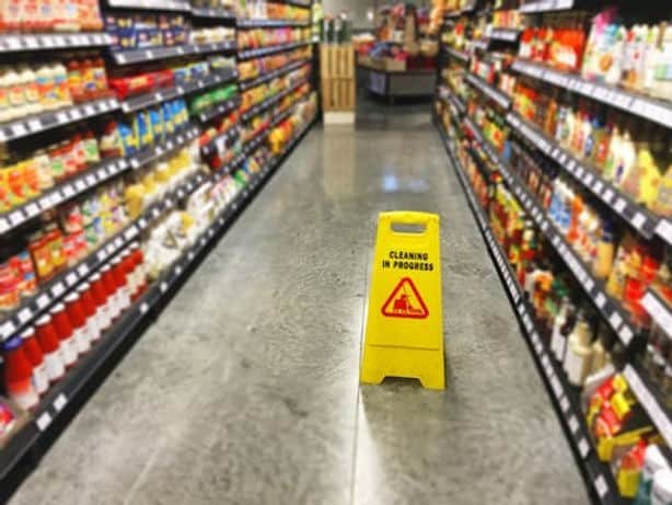 A yellow "Cleaning in Progress" sign stands in the aisle of a grocery store between shelves stocked with various products.