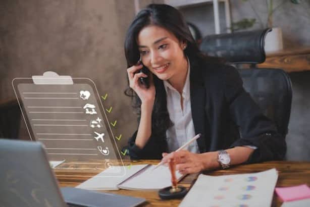 A woman in business attire sits at a desk, talking on the phone, taking notes, and looking at a laptop with a transparent digital checklist overlay.