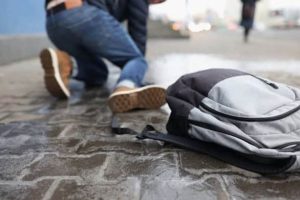 Person kneeling on wet pavement with a gray and black backpack on the ground nearby.