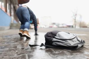 A person in winter clothing slips and falls on an icy sidewalk, leaving a backpack behind.
