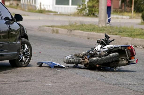 A motorcycle is lying on its side next to a car on a city street, indicating a recent collision.