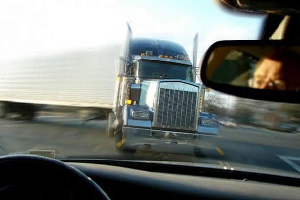View from inside a car as a large semi-truck appears to be skidding or jackknifing directly toward the vehicle on a road.