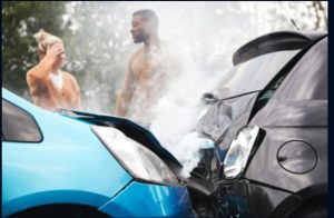 Two cars are involved in a front-end collision, with smoke rising from the impact. Two people stand nearby, one holding their head in apparent distress.