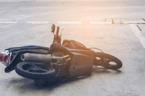 A fallen motorcycle lies on its side on a paved road, with the exhaust and rear wheel visible.