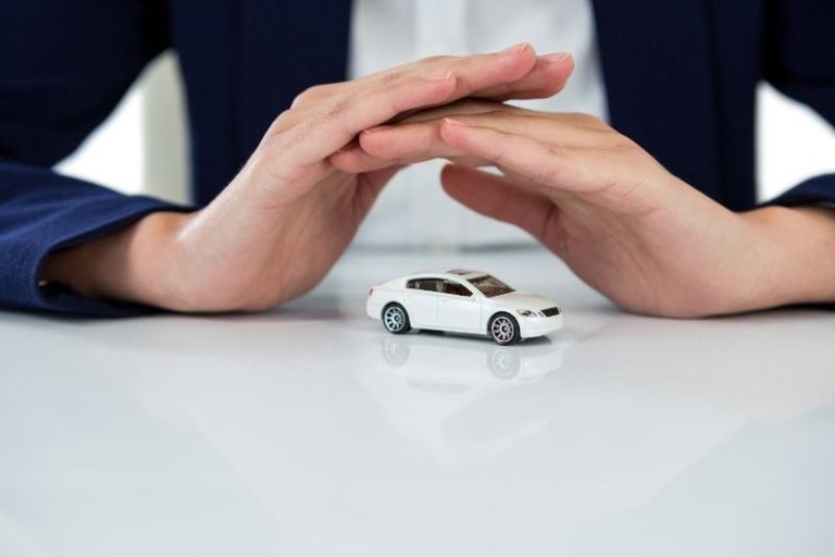 Person cupping hands protectively over a small white toy car on a white surface.