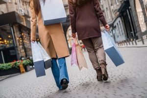 Two people walking down a city street, carrying multiple shopping bags in their hands and over their shoulders.